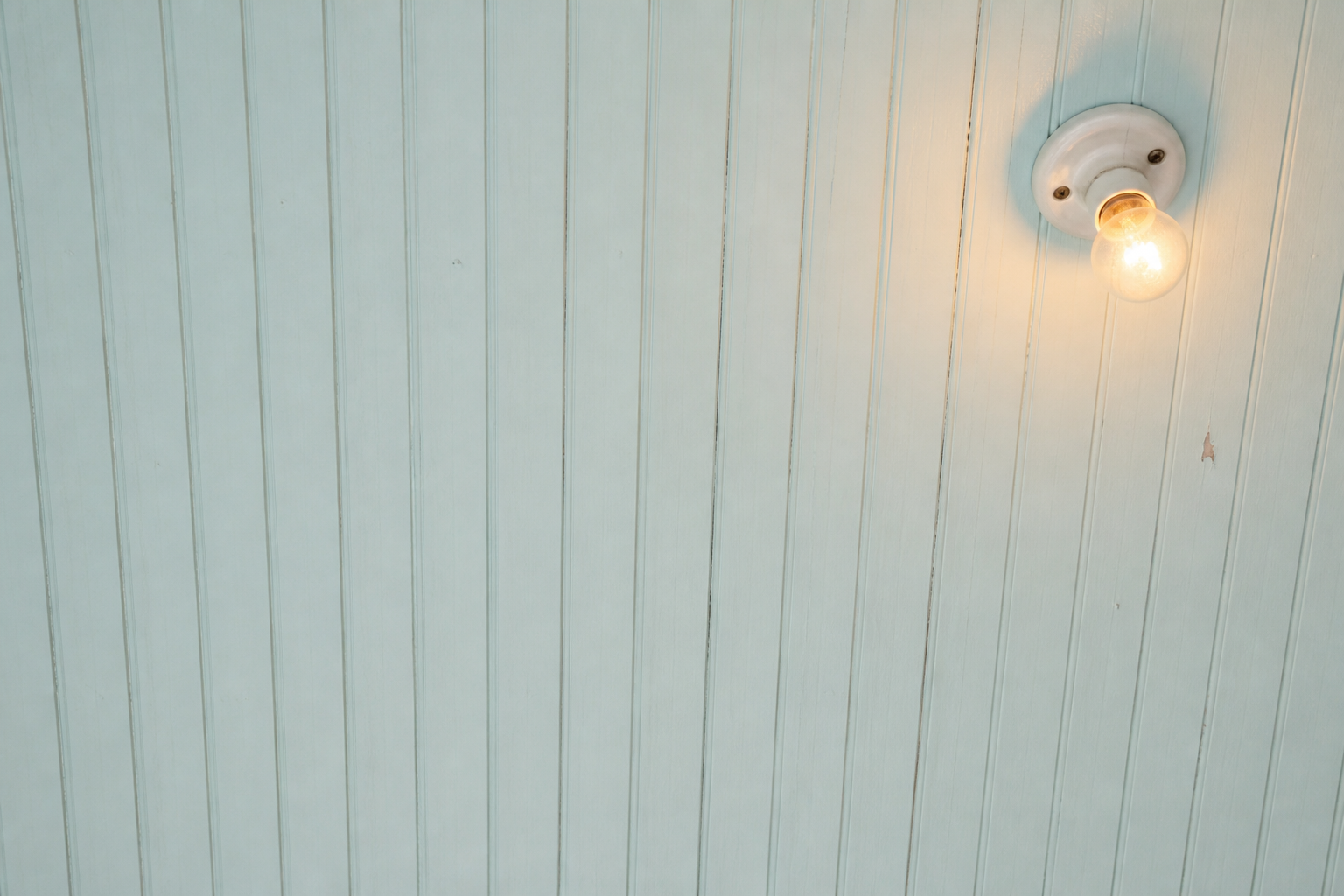 A porch ceiling of beadboard painted pale haint blue, with a single warm bulb lit.